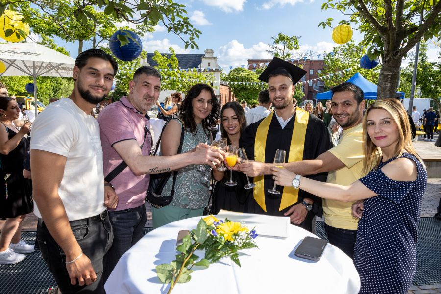 Mehrere Absolvent*innen der Viadrina stoßen auf dem Campus auf ihren Abschluss an, blauer Himmel im Hintergrund